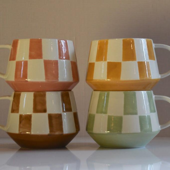 Two sets of checkered ceramic mugs stacked on a reflective surface with a neutral background