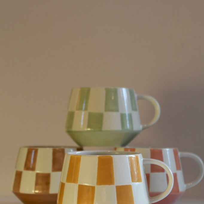 Set of ceramic mugs with checkered patterns on a reflective surface.