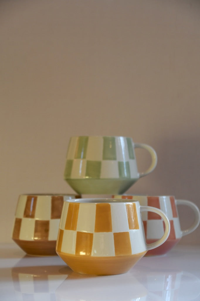 Set of ceramic mugs with checkered patterns on a reflective surface.