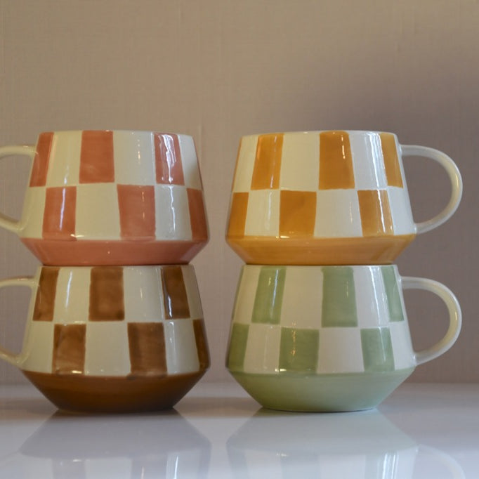 Set of four checkered ceramic mugs stacked on a reflective surface with a neutral background