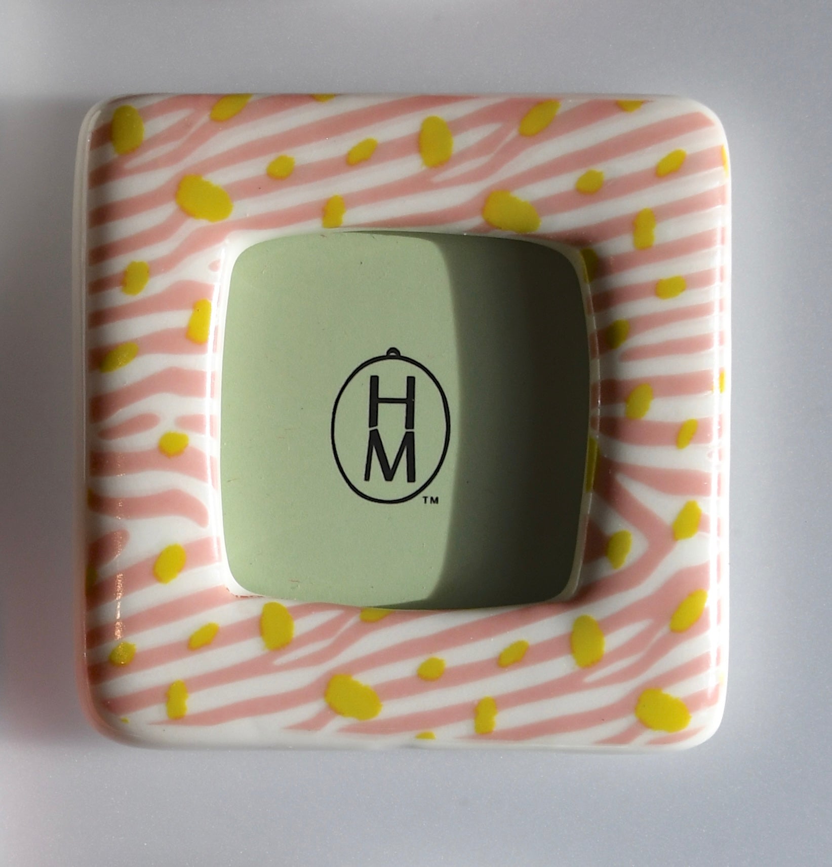 Square frame with pink and yellow pattern and green center featuring 'HM' logo on a gray background