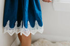 This sleeveless blue denim dress features a playful ruffle neckline and intricate lace hemline