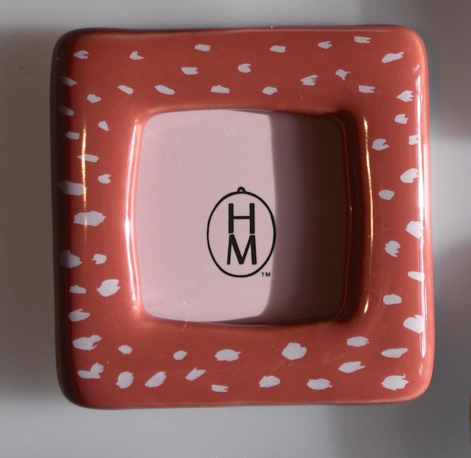 Ceramic frame with white pattern and 'H&M' logo on a plain background