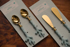 Set of gold and blue spoons and spreaders on branded cards on a wooden surface