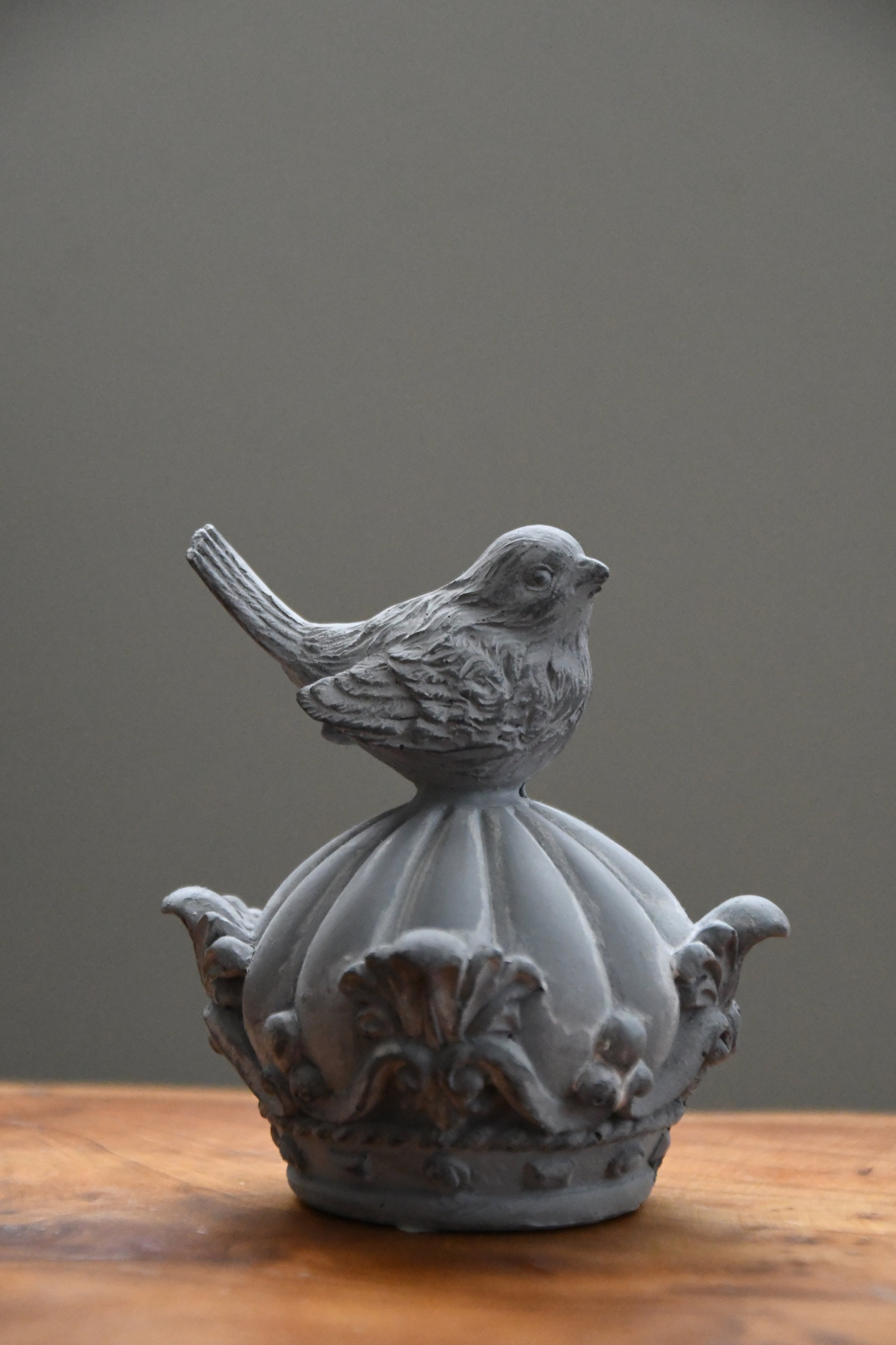 Decorative bird sculpture on a pedestal against a gray background