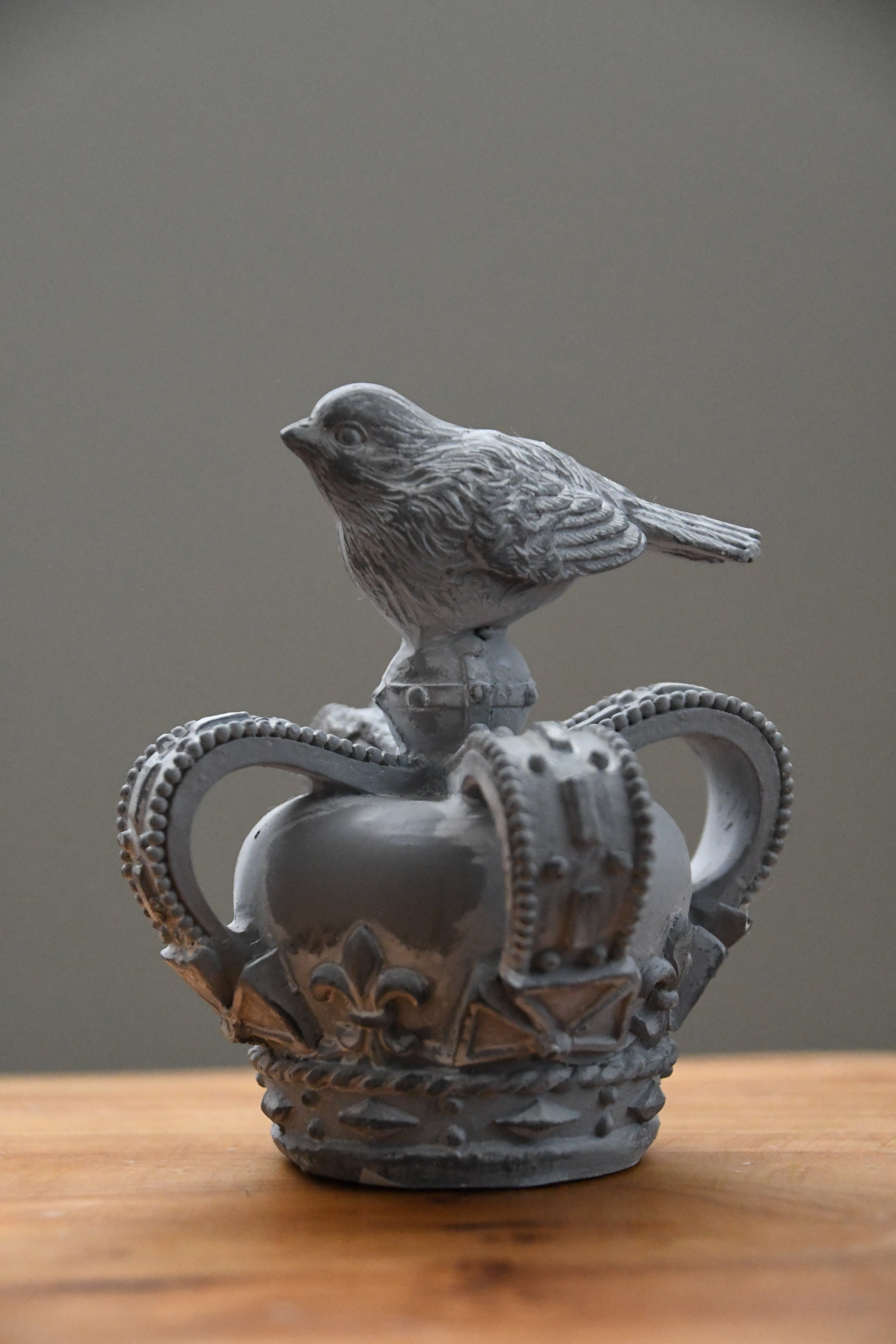 Decorative object resembling a crown with a bird on top, placed on a wooden surface.