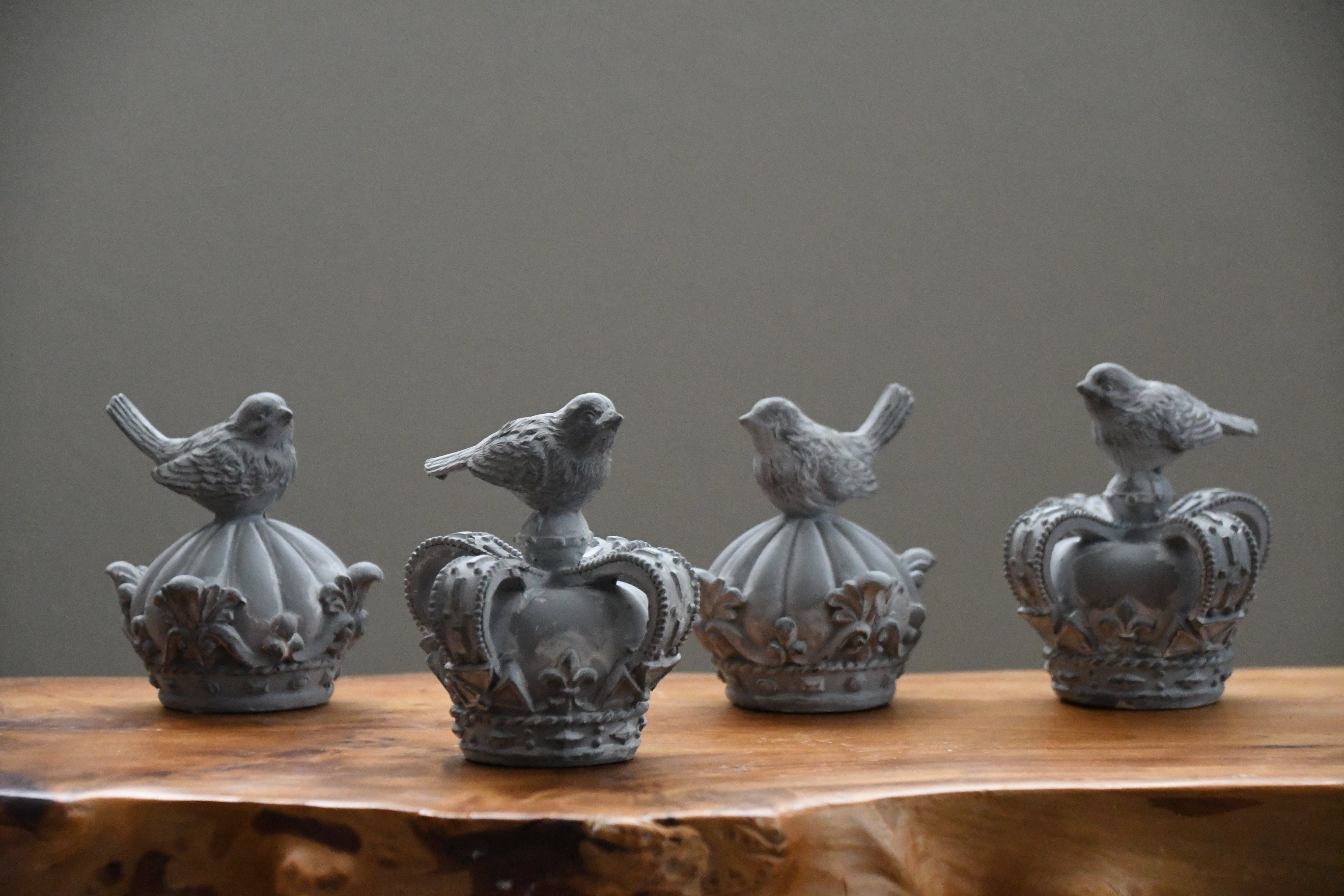 Decorative bird sculptures on crowns on a wooden surface with a gray background