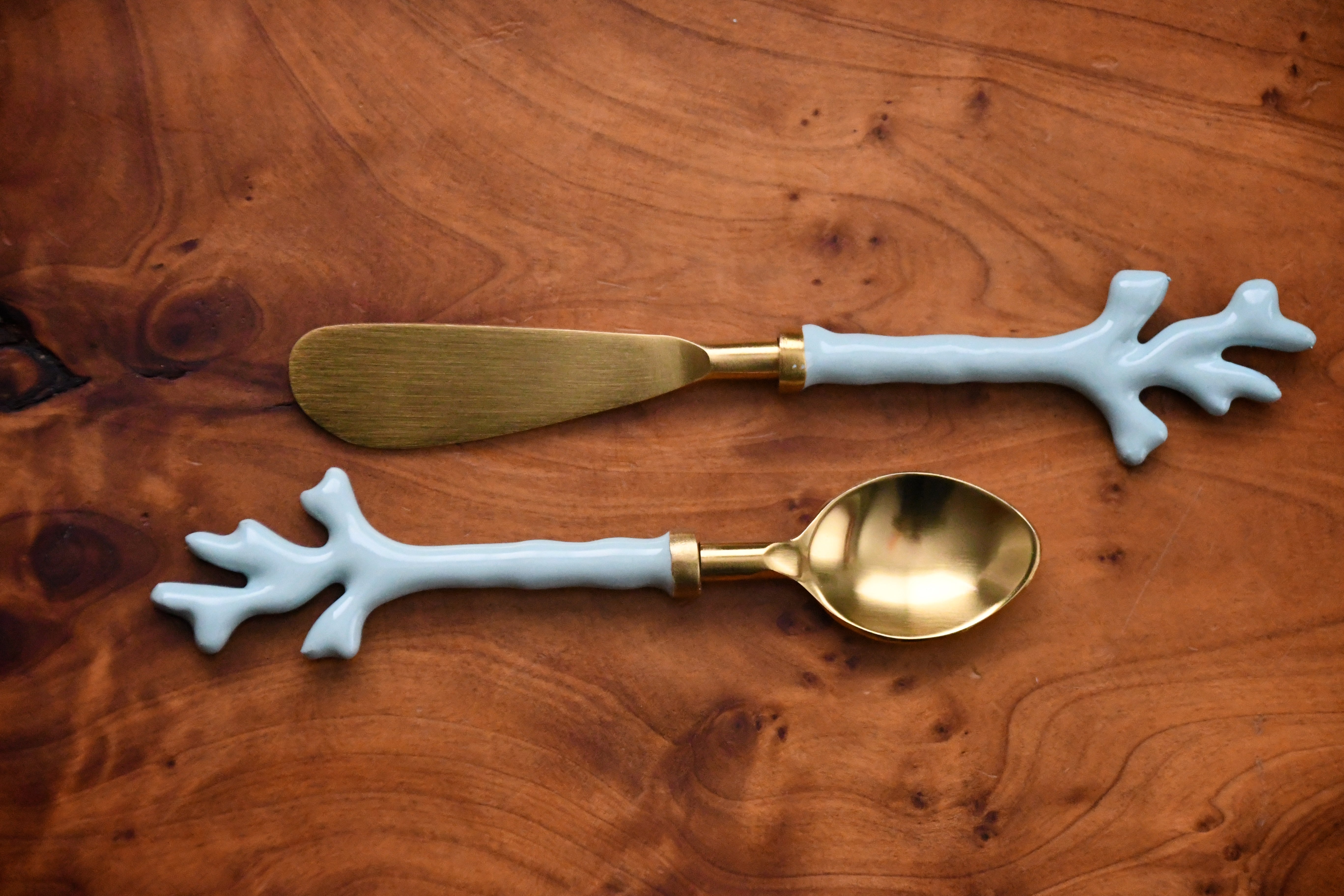 Gold spoon and butter knife with white coral-like handles on a wooden surface