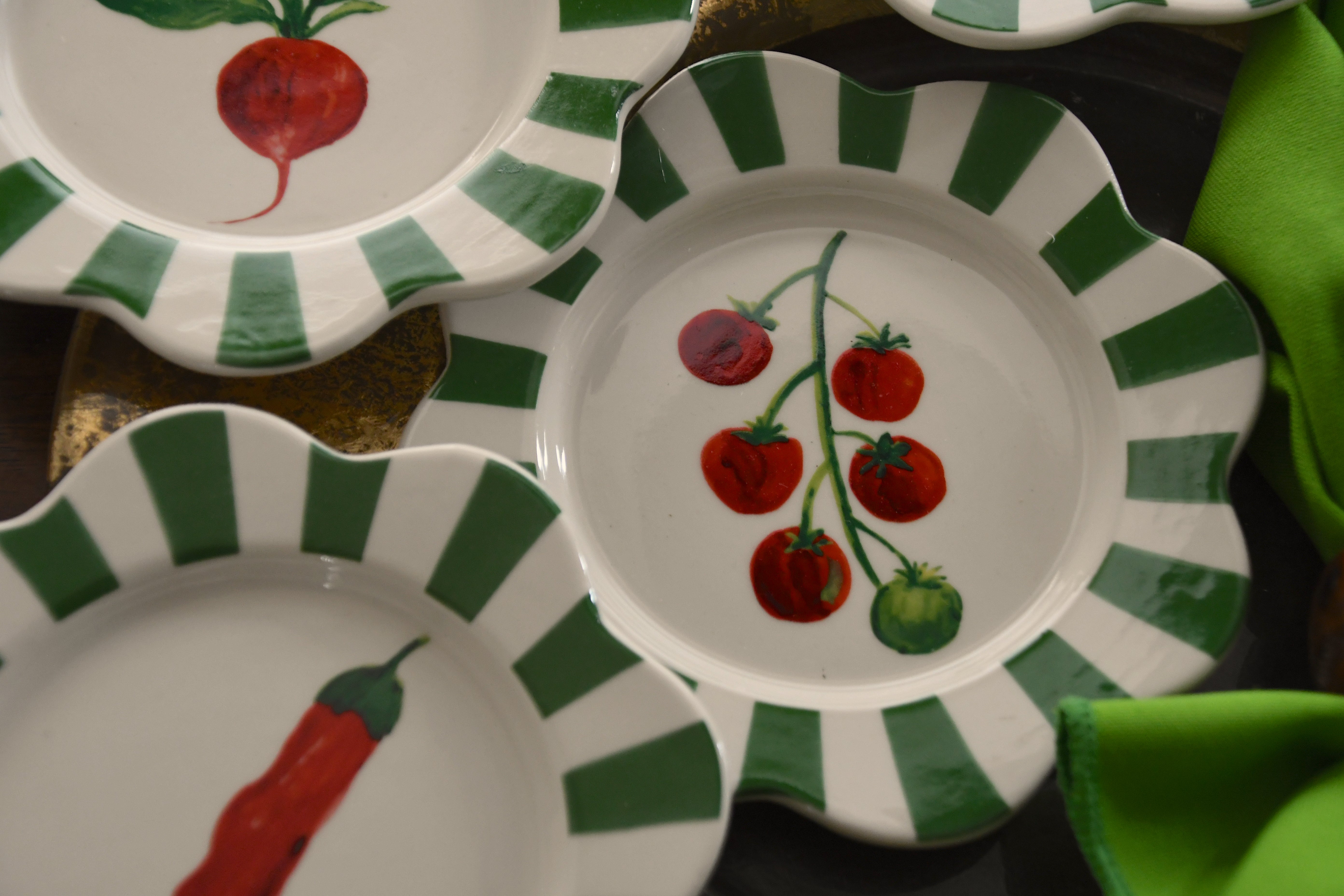 Set of ceramic plates with green stripes and colorful illustrations on a dark surface.