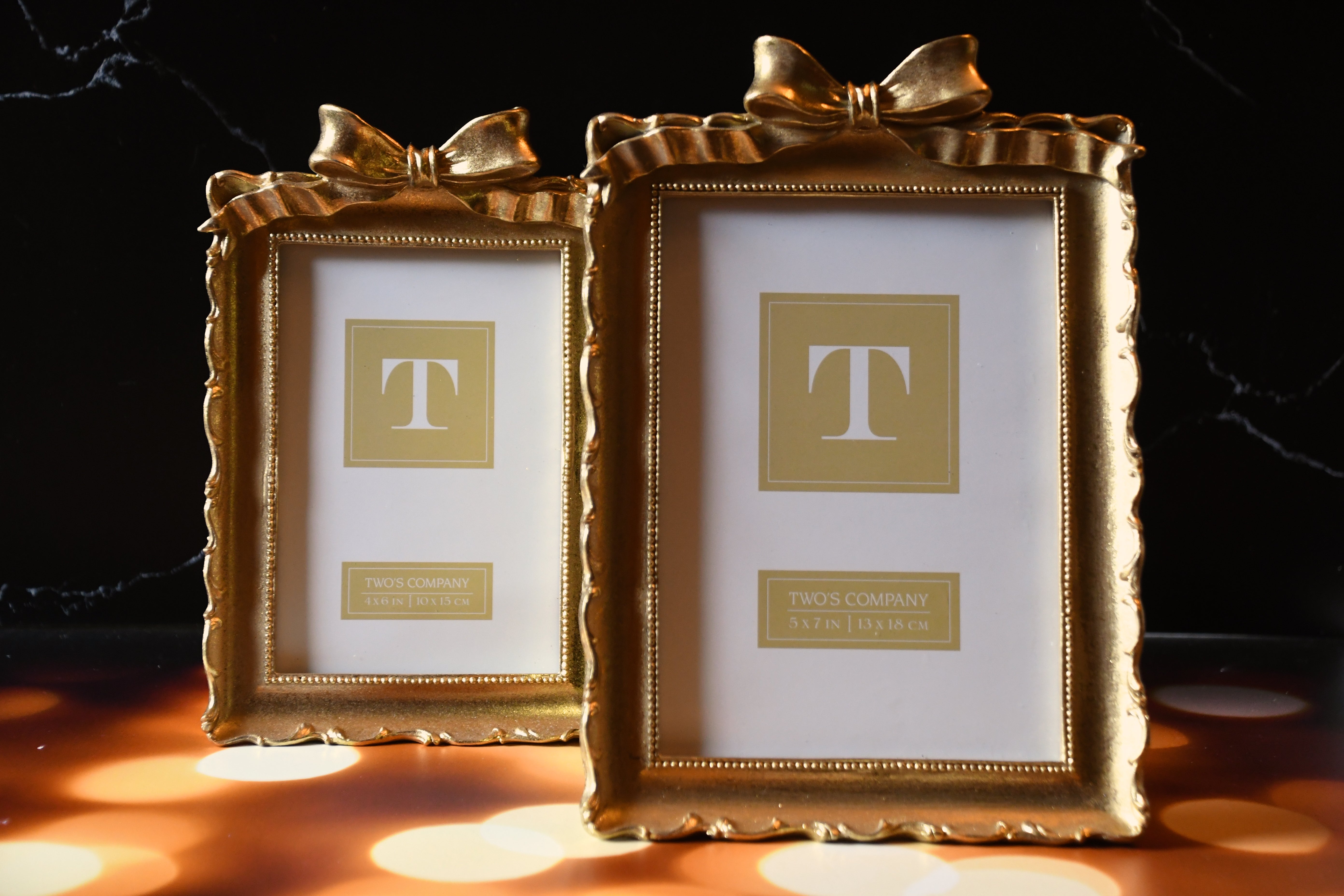 Two gold picture frames with decorative bows on a dark background