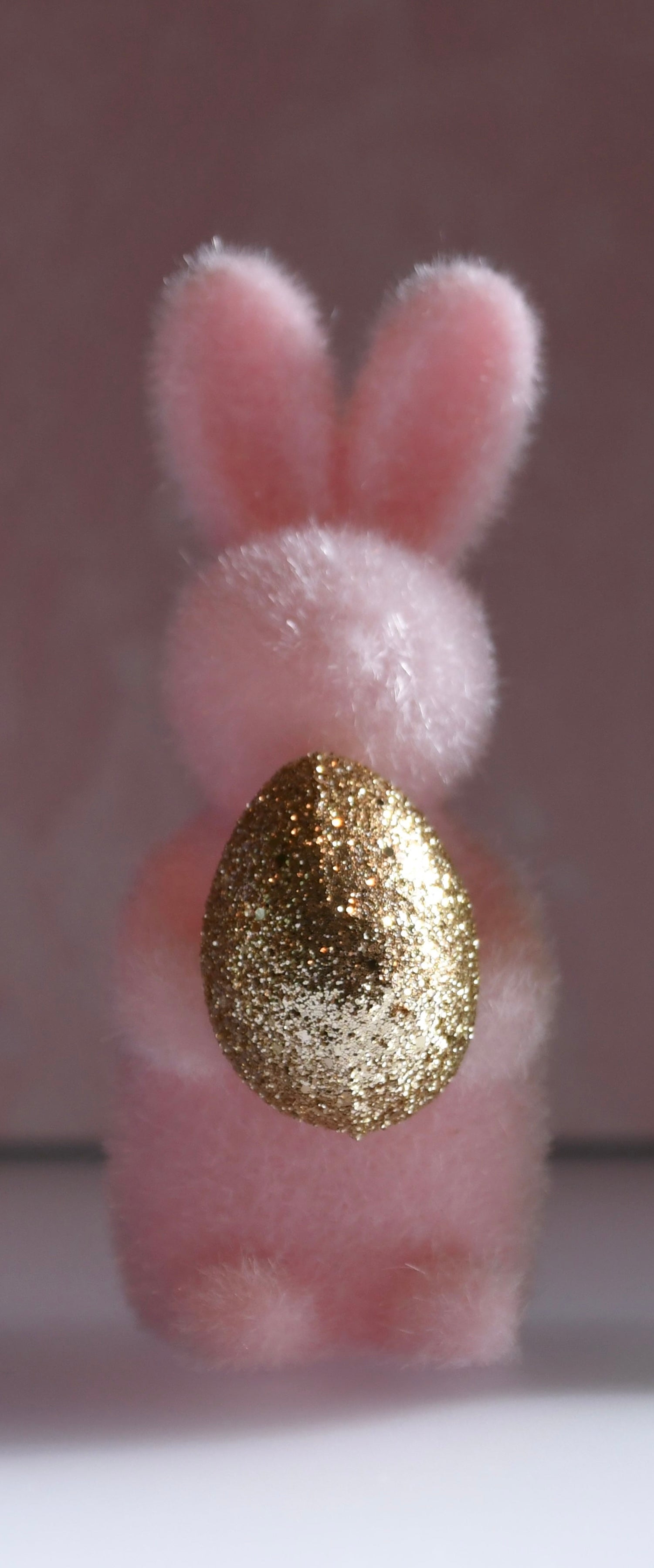 Pink plush bunny with a gold glittery egg on a blurred background