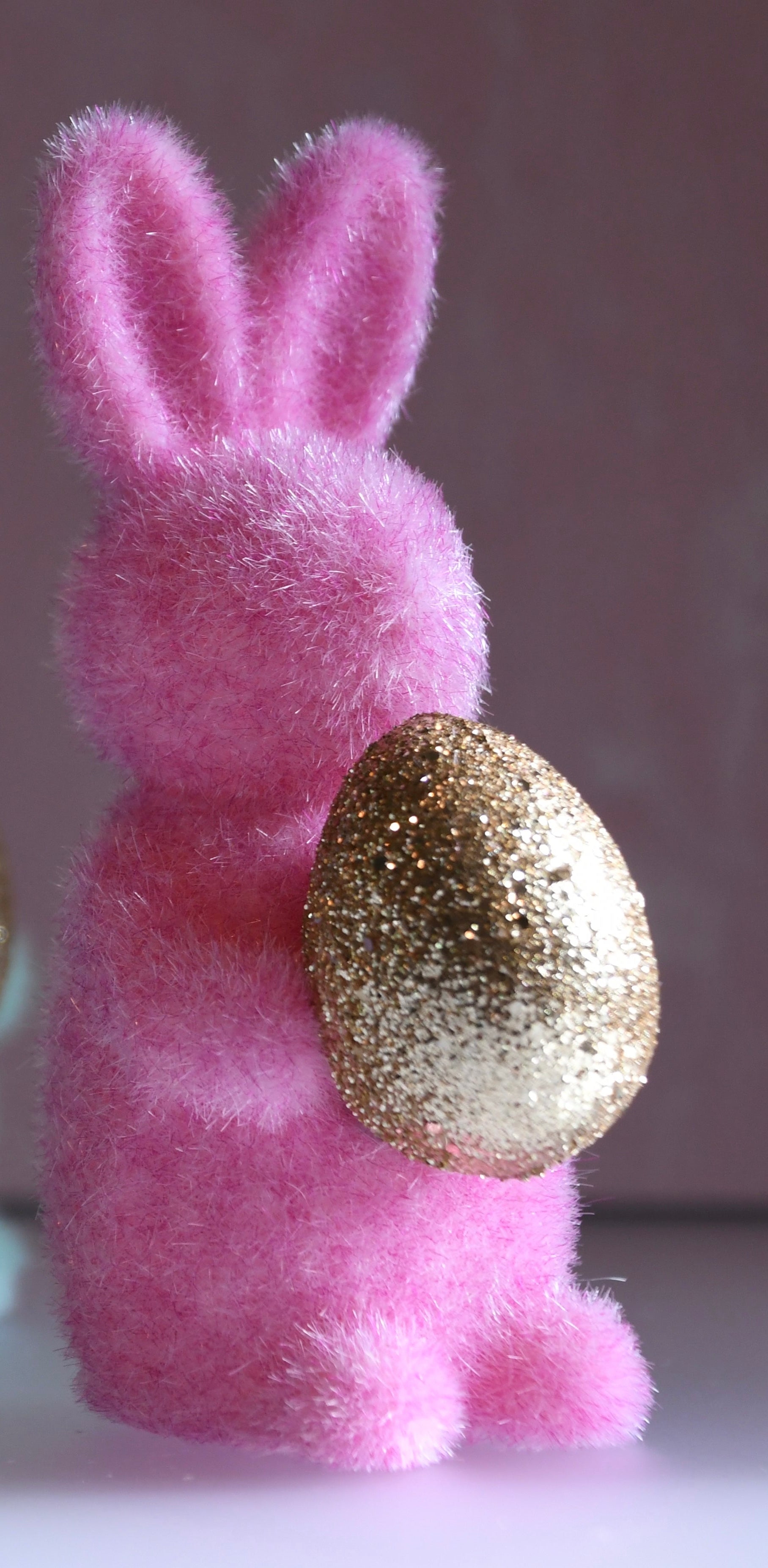 Pink fluffy bunny with a gold glittery egg on a neutral background