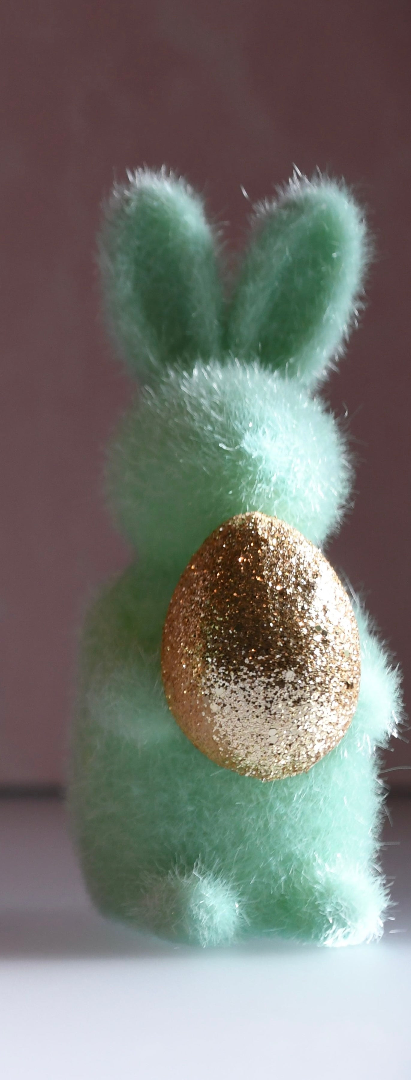 Green felt bunny with a gold glittery egg on a plain background