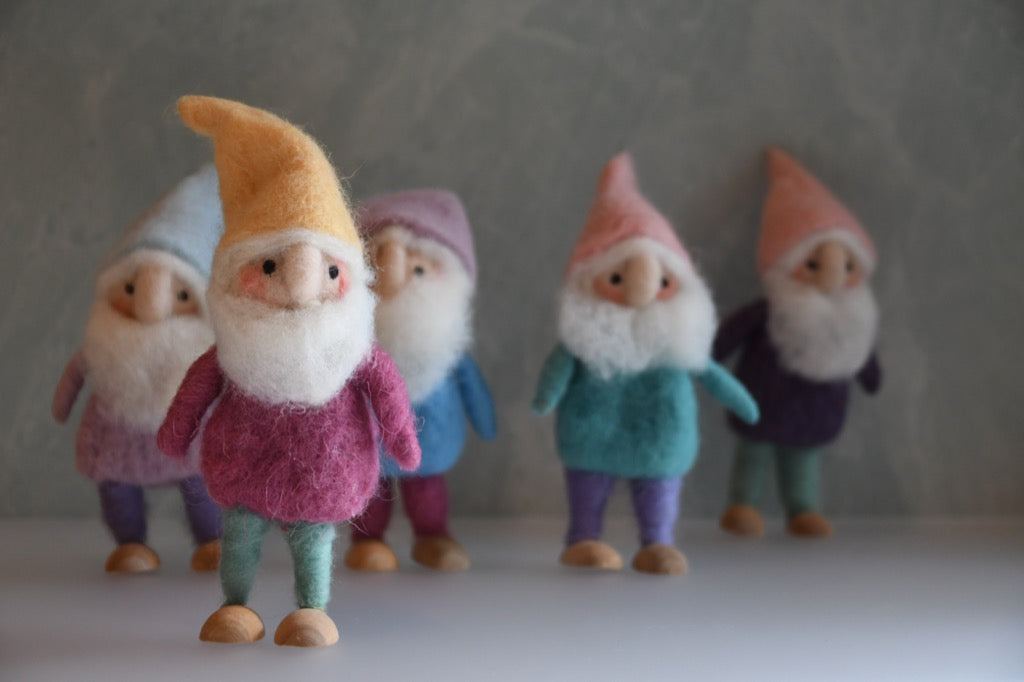 Five colorful gnome figurines with different colored hats and outfits on a neutral background
