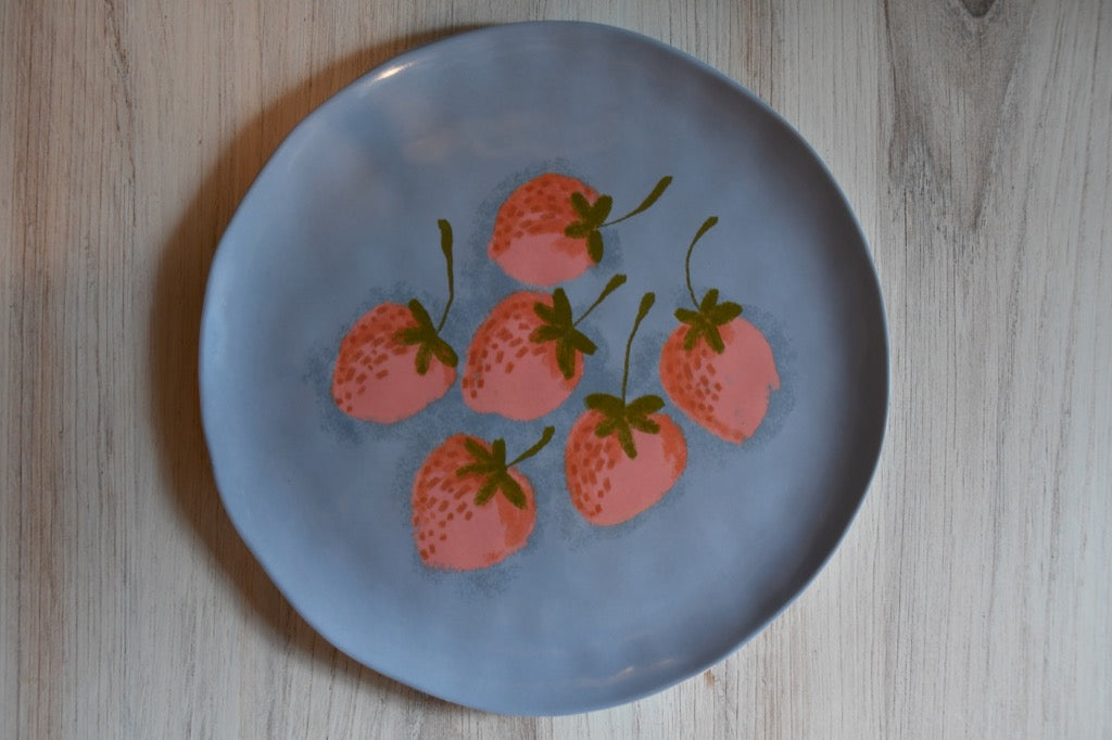 Blue plate with pink strawberry design on a wooden surface