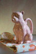 Pink ceramic cat-shaped pitcher on a colorful cloth with a neutral background