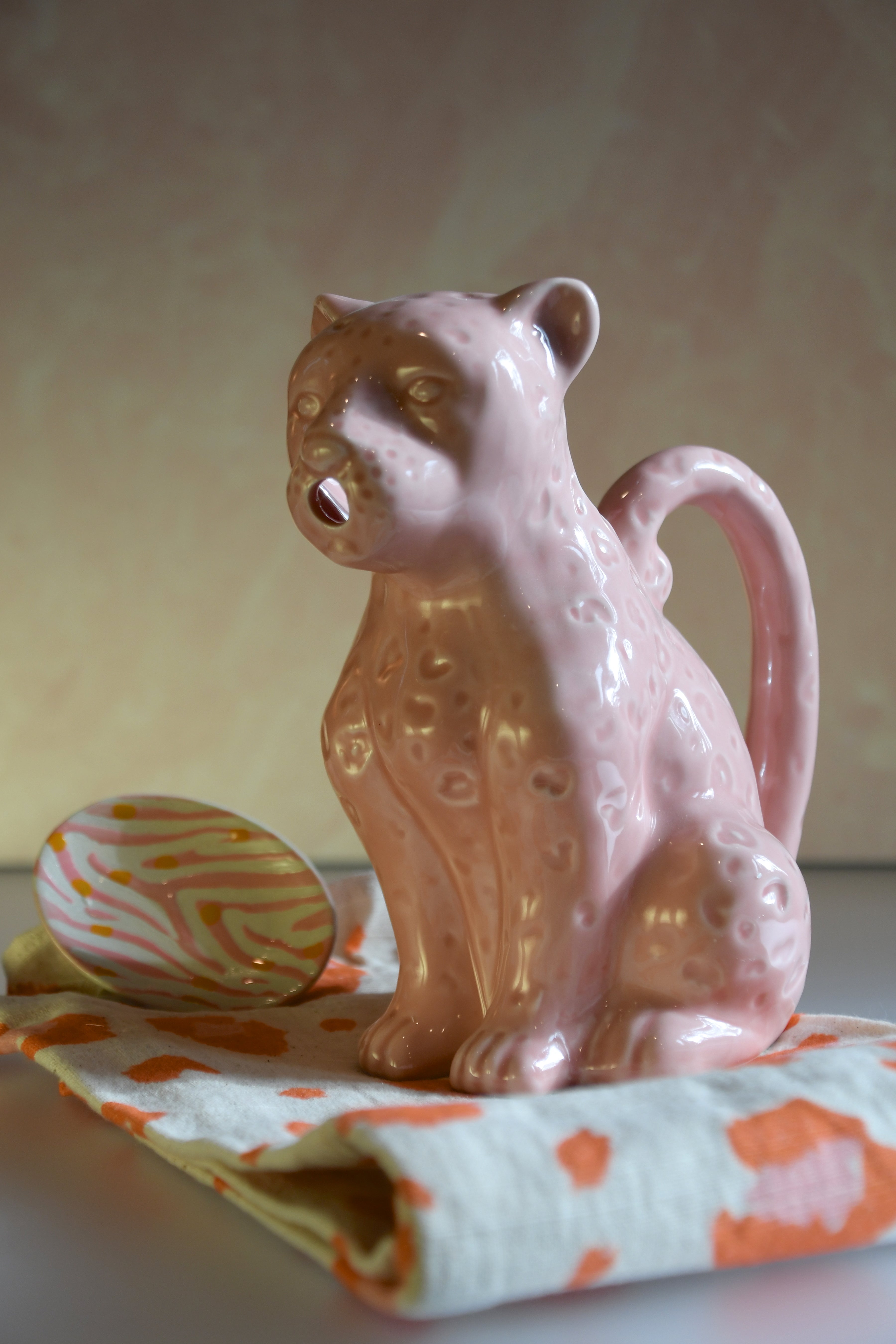 Pink ceramic cat-shaped pitcher on a colorful cloth with a neutral background