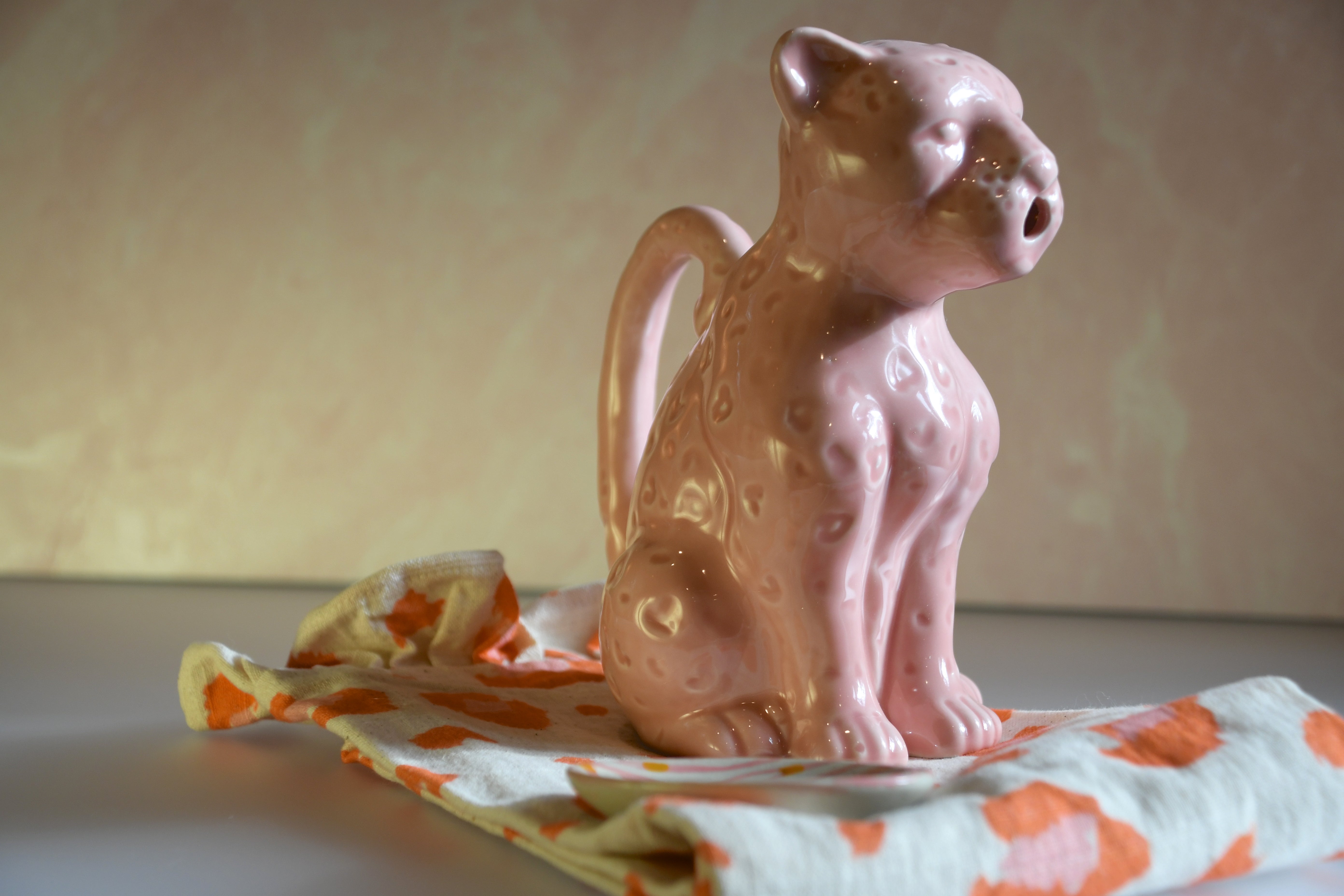 Pink ceramic animal-shaped pitcher on a colorful cloth with a blurred background
