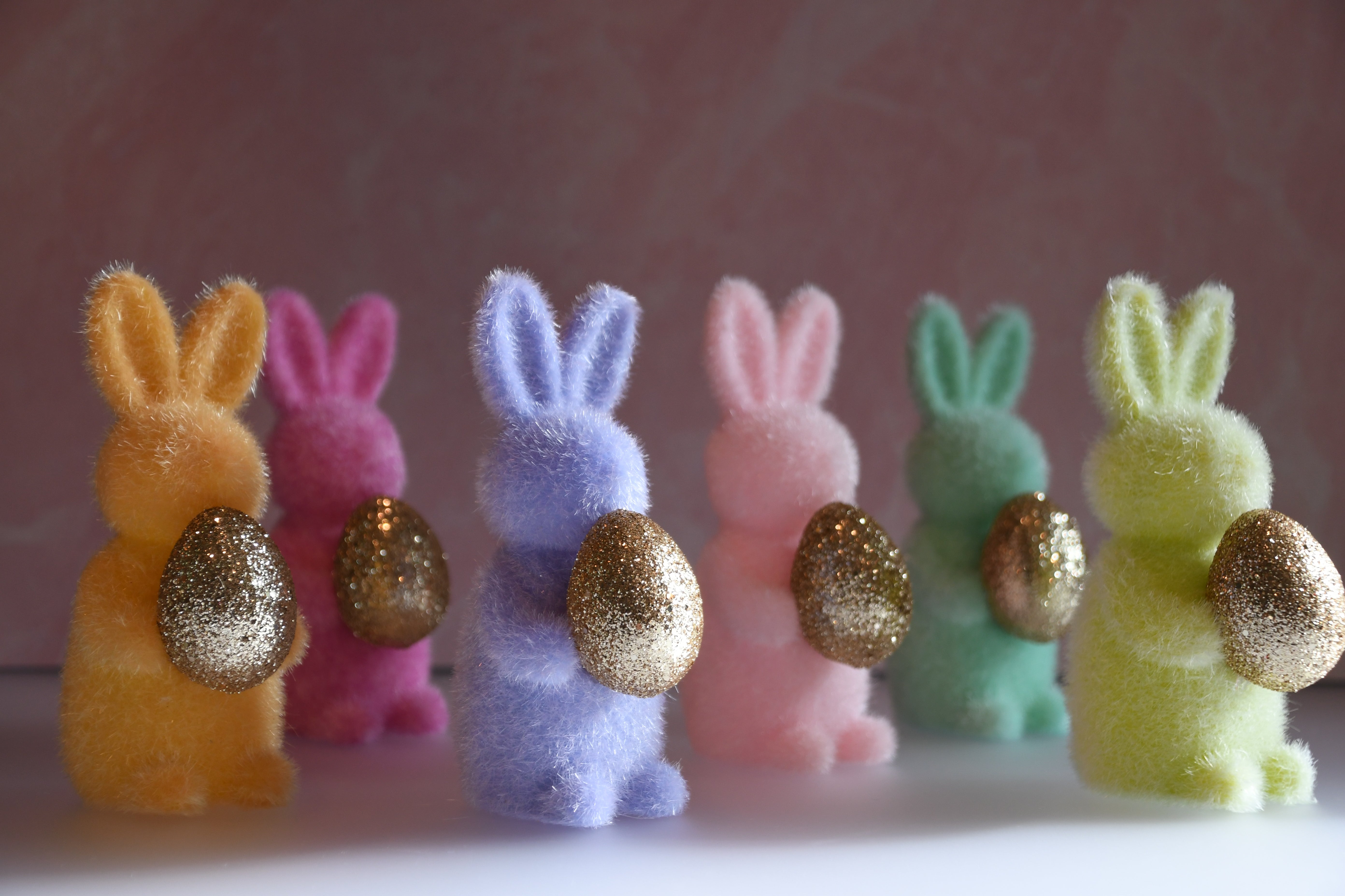 Colorful foam bunny figurines with glittery eggs on a pink background