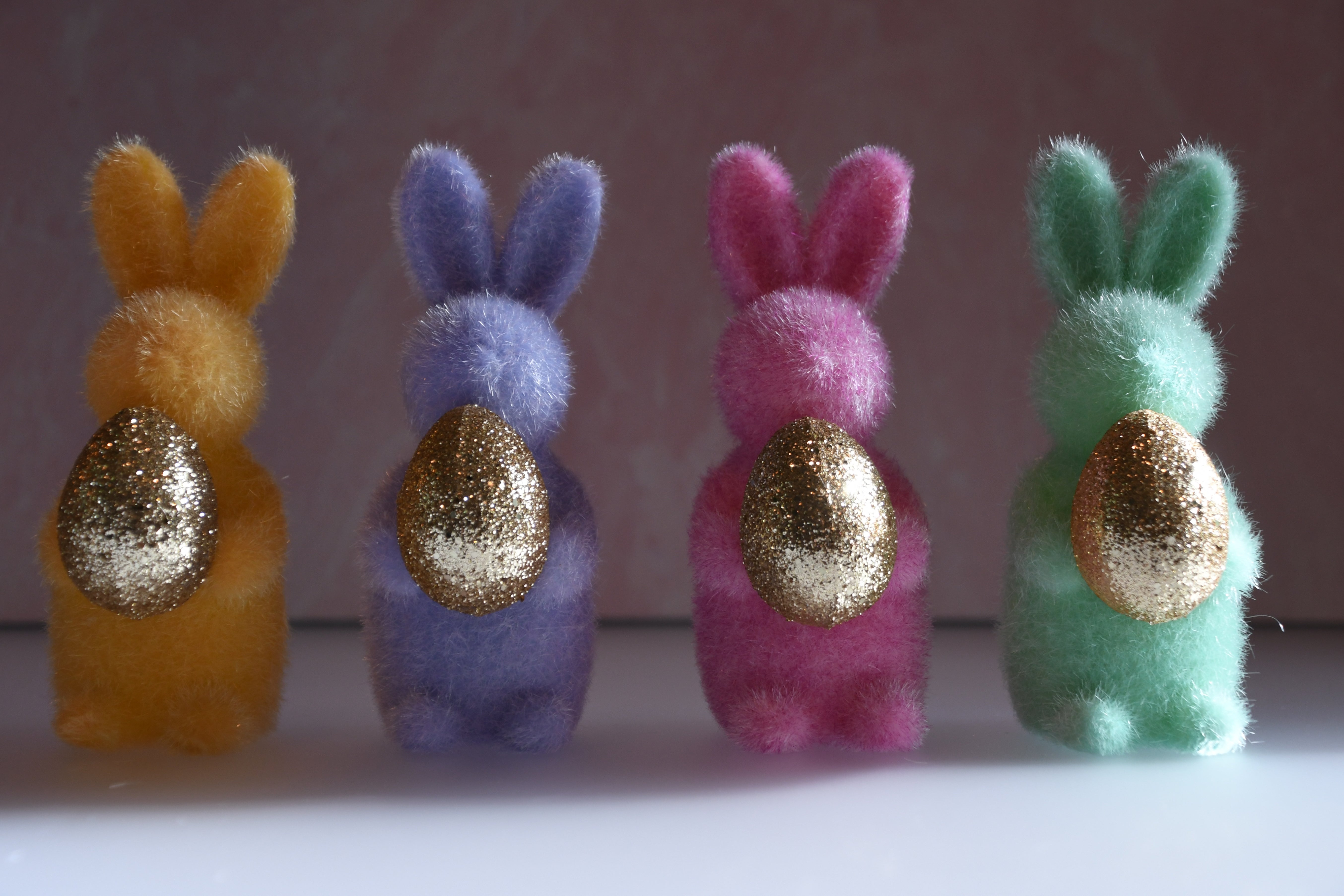 Four colorful bunny figurines with gold eggs on a plain background