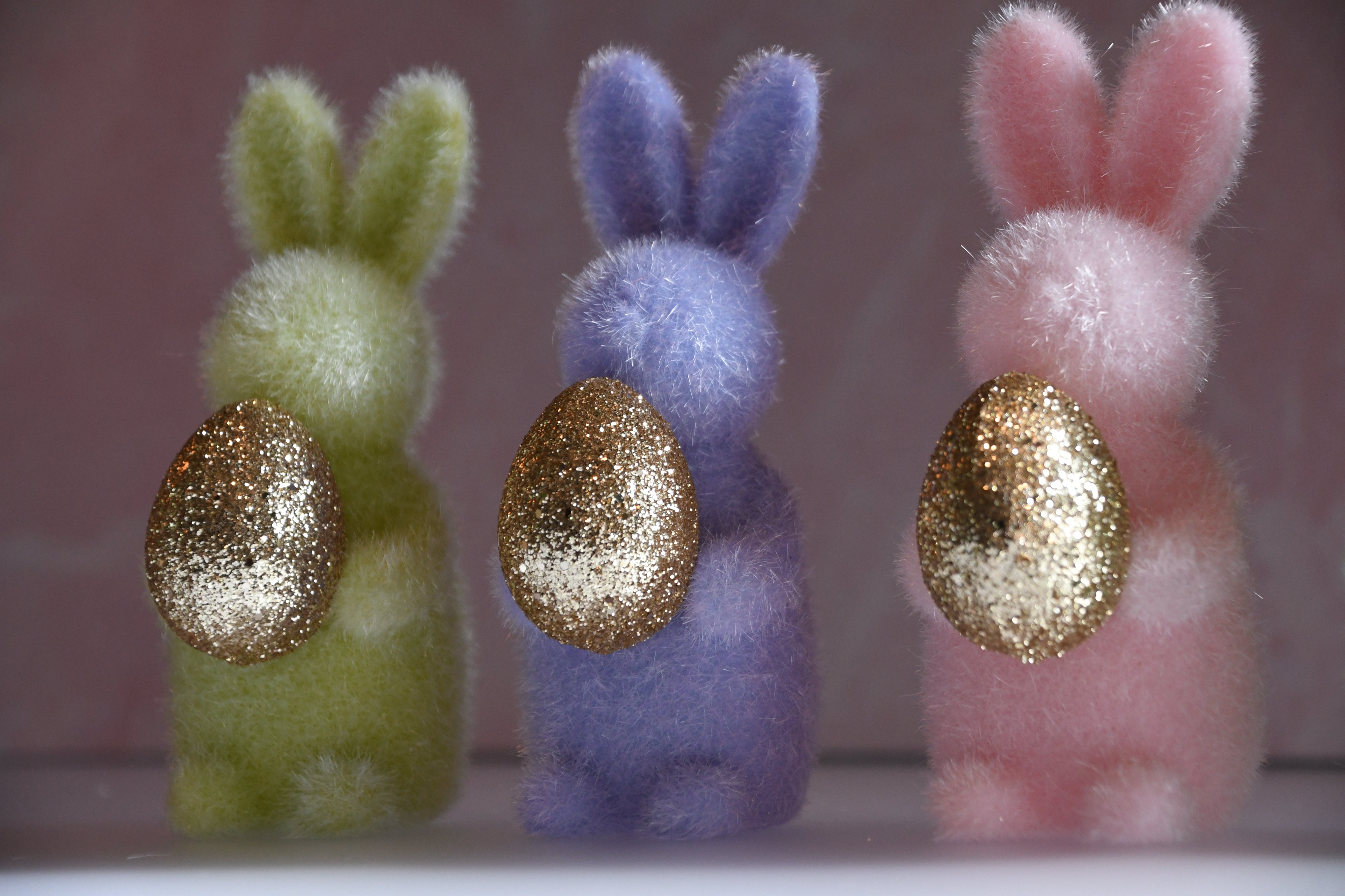 Three fluffy bunny toys with glittery golden eggs on a blurred background