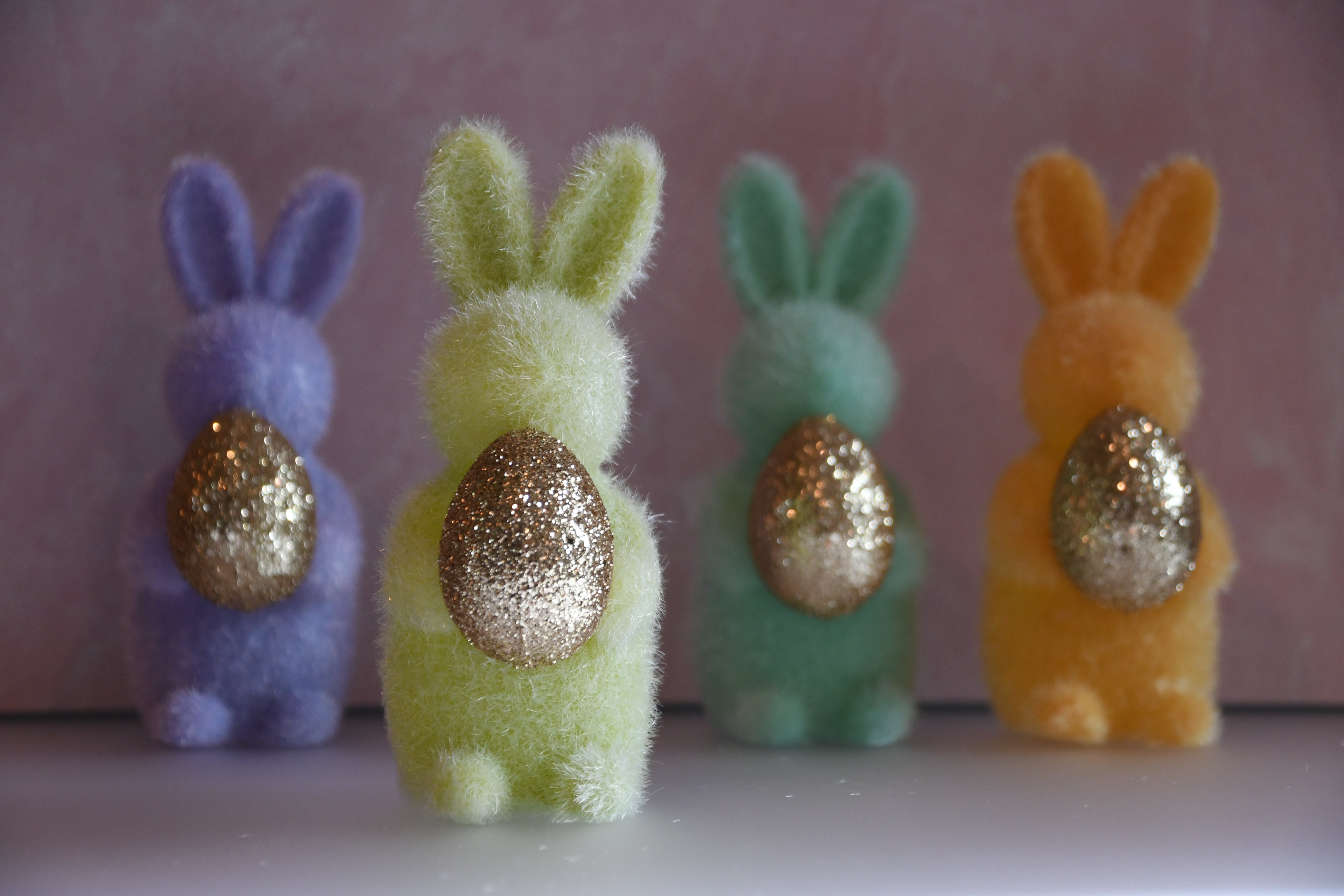Four colorful bunny figurines with glittery eggs on a pink background