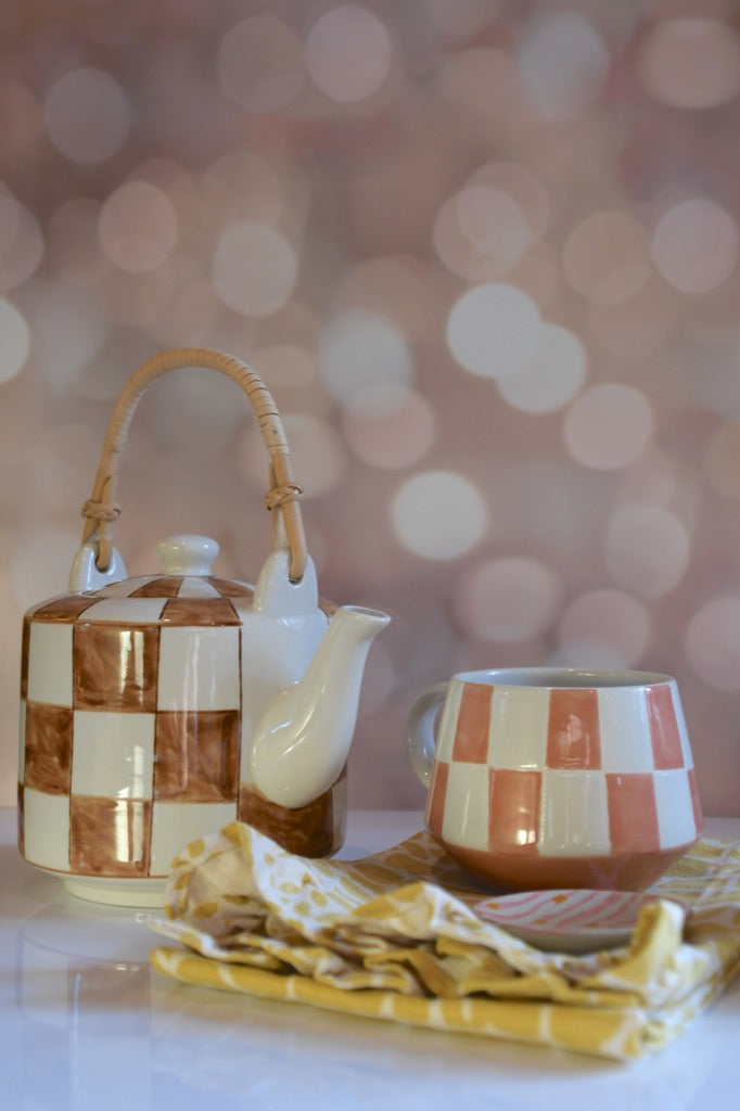Ceramic teapot and mug with checkered pattern on a blurred bokeh background