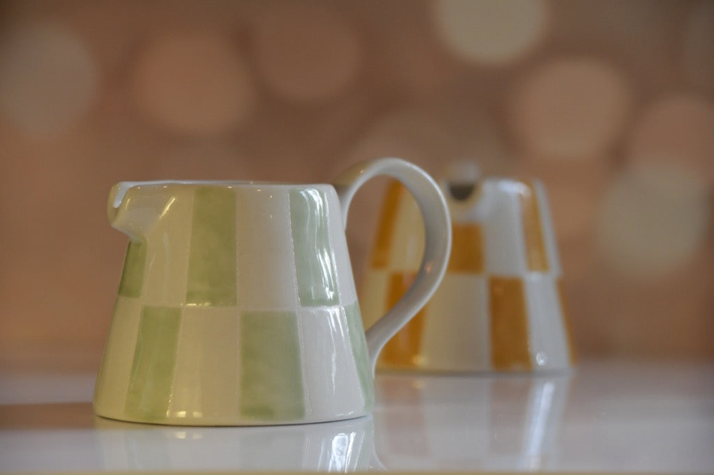 Green and white striped ceramic pitcher on a blurred background