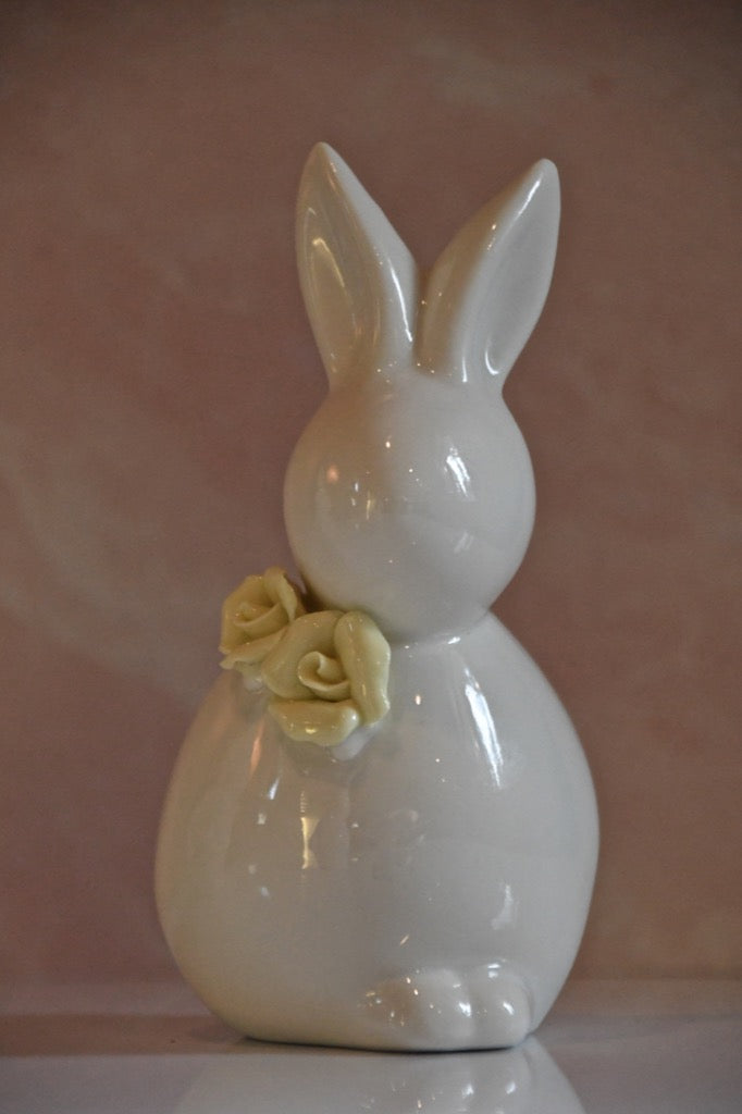White ceramic bunny figurine with a yellow rose on a pink background