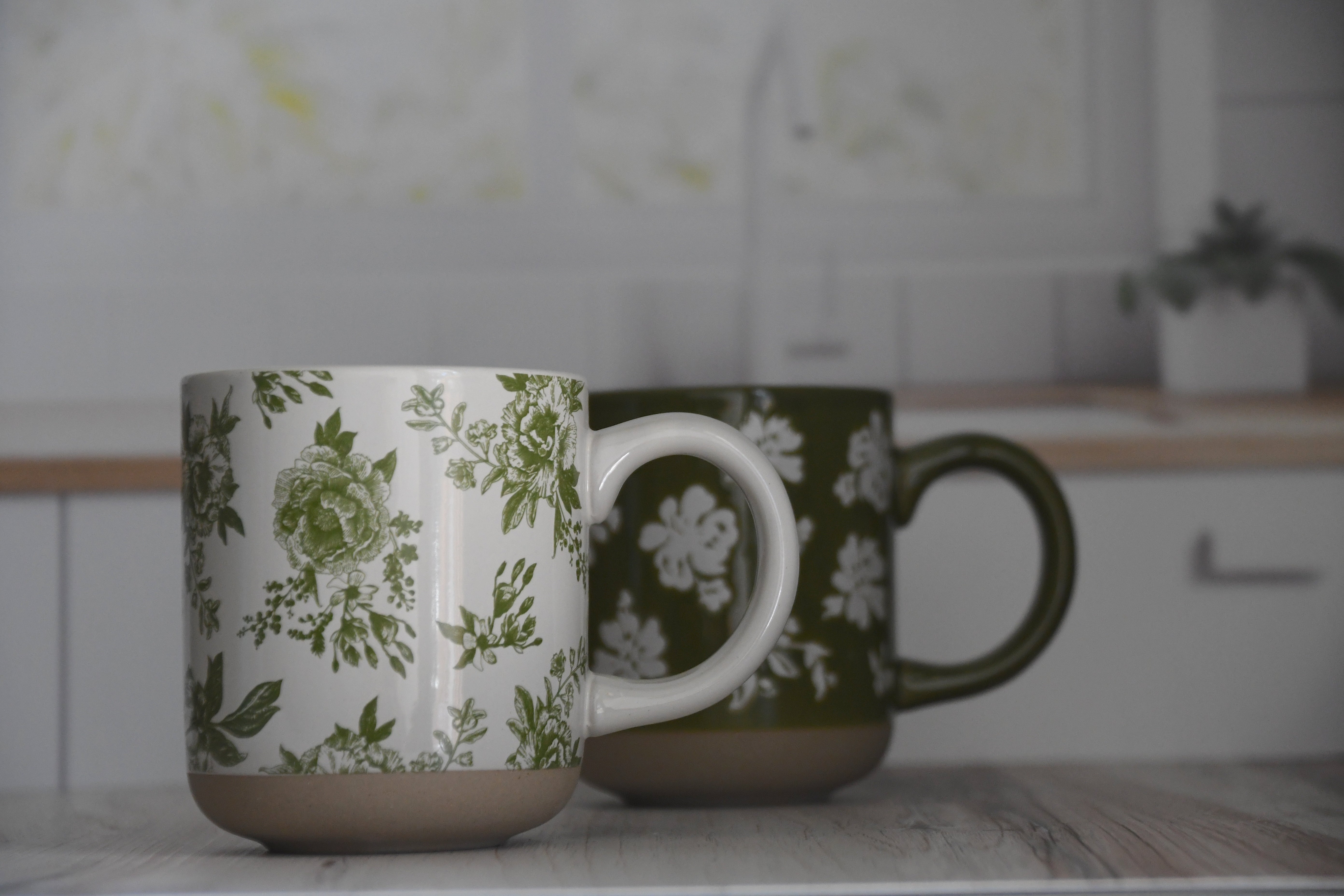 Two ceramic mugs with floral patterns on a kitchen counter.