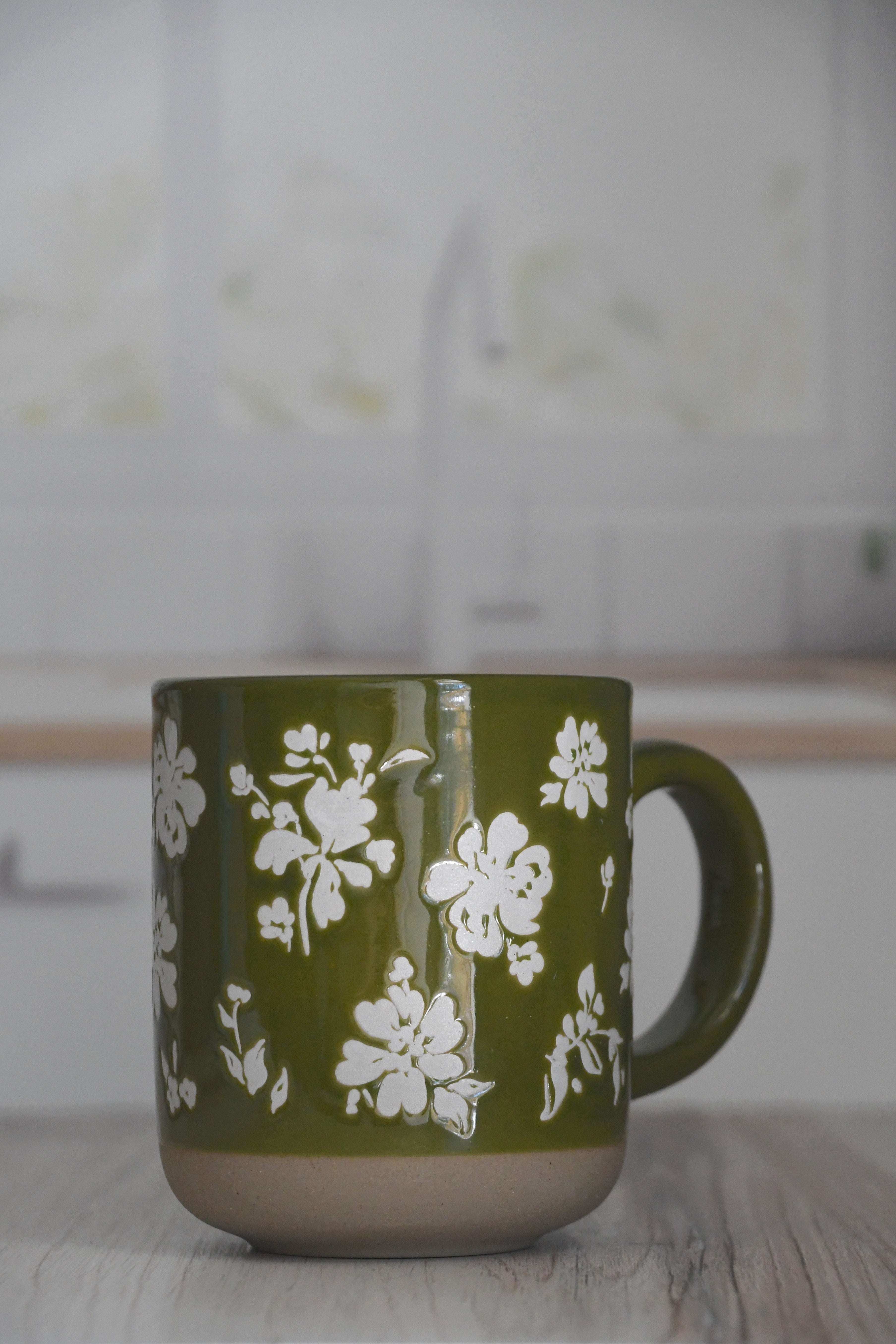 Green mug with white floral pattern on a wooden surface