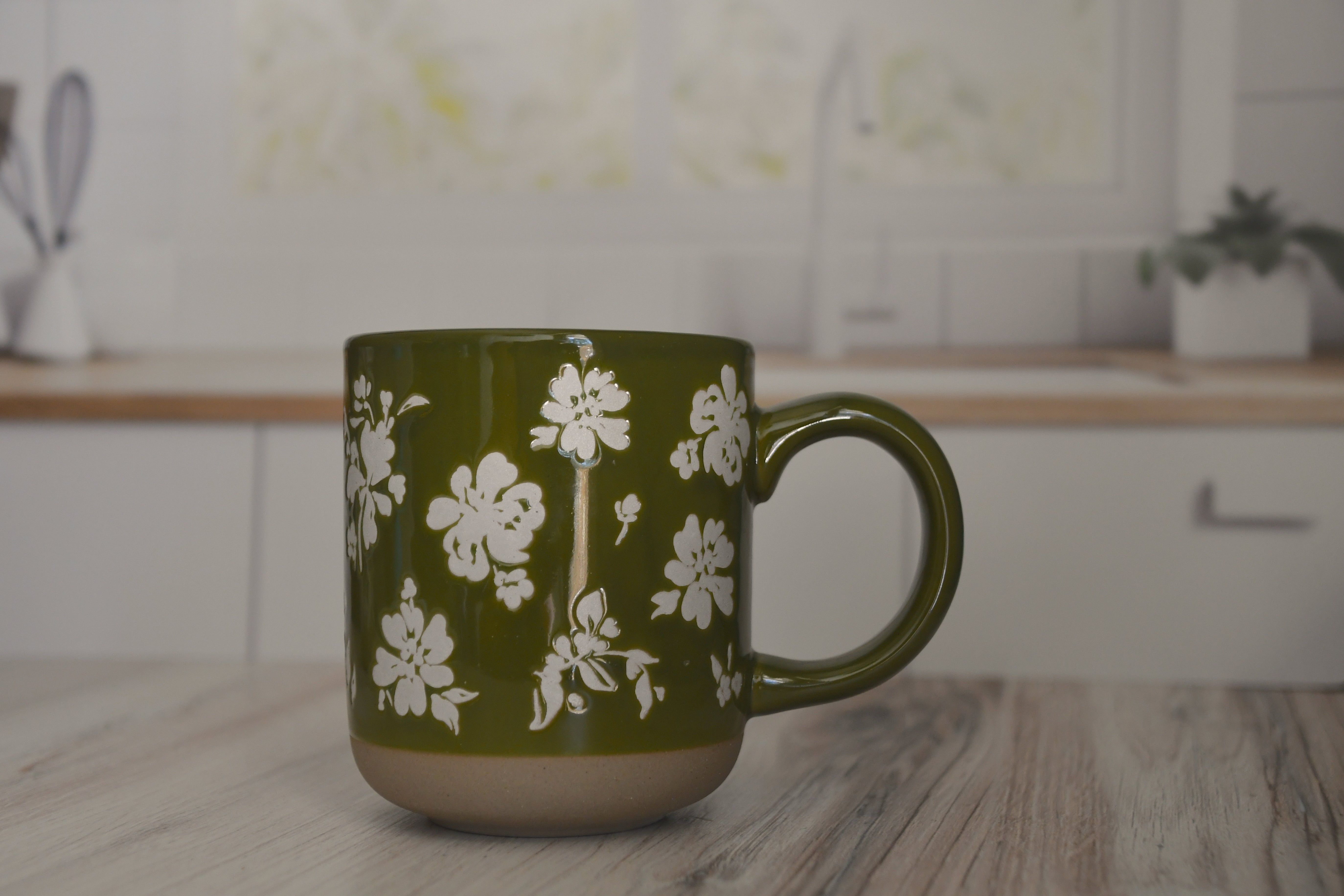 Green mug with white floral pattern on a kitchen counter