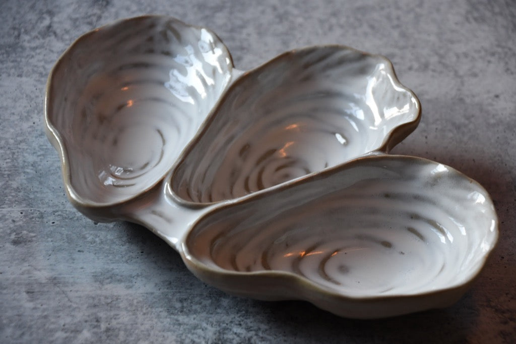 Three-section ceramic dish shaped like oyster shells on a gray surface