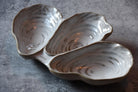 Three-section ceramic dish shaped like oyster shells on a gray surface