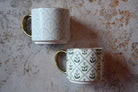 Two patterned mugs on a textured surface
