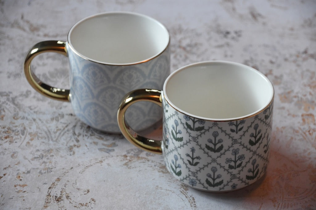Two patterned mugs with gold handles on a textured surface