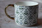 White mug with floral pattern and gold handle on a textured surface