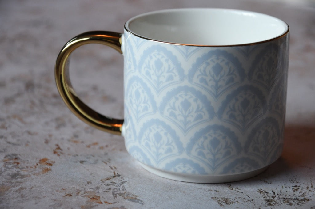 Ceramic mug with gold handle and blue geometric pattern on a textured surface