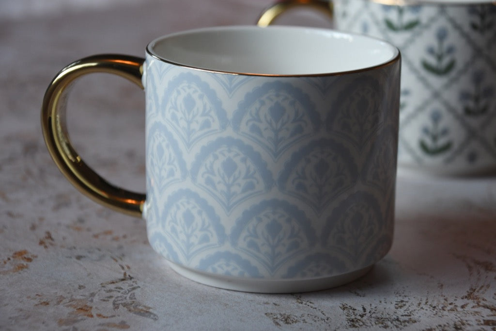 Patterned ceramic mug with gold handle on a textured surface