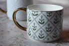 White mug with floral pattern and gold handle on a textured surface