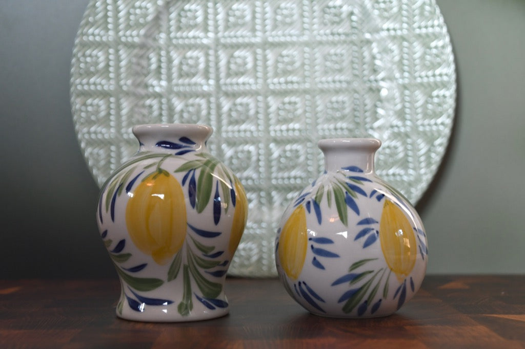 Two ceramic vases with lemon design on a wooden surface with a textured wall in the background.