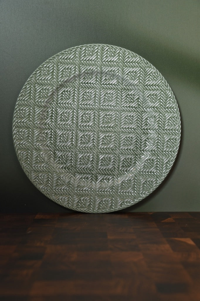 Round textured green rug on a dark surface with a green wall background