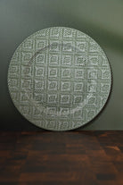 Round textured green rug on a dark surface with a green wall background