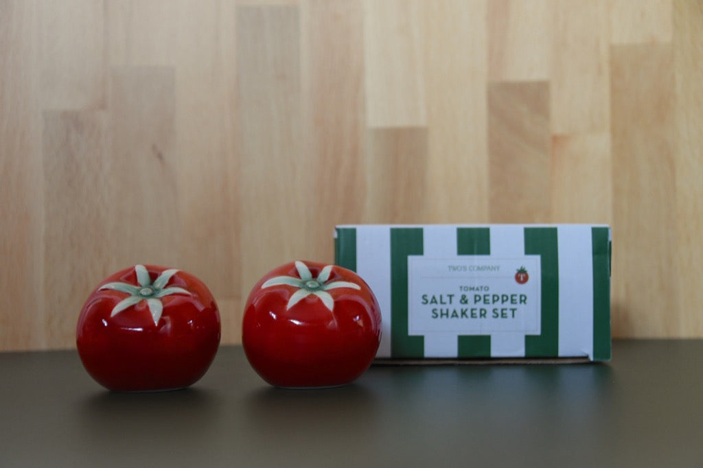 Tomato-shaped salt and pepper shakers with a matching box on a wooden surface.