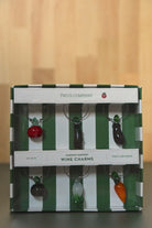 Two's Company Garden Harvest wine charms in a striped box on a wooden surface.