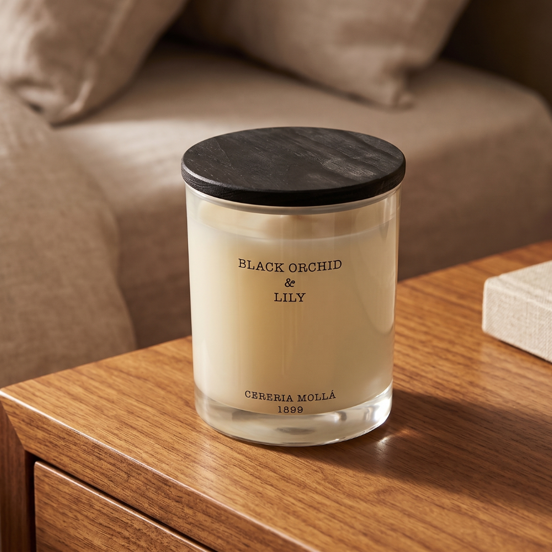 Candle labeled 'Black Orchid & Lily' on a wooden surface with a blurred sofa in the background