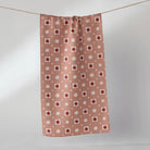 A rectangular dust cloth or curtain with a repeating pattern of red apples and white pumpkins on a dusty pink background, hanging from a string against a light gray wall.