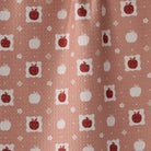 A close-up of a fabric or wallpaper pattern featuring red apples and white pumpkins on a dusty terracotta background.