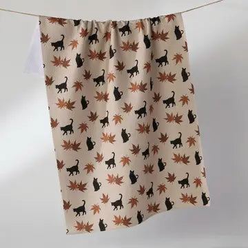 A beige curtain panel hanging from a thin line, featuring a repeating pattern of black cat silhouettes and brown and orange autumn maple leaves.
