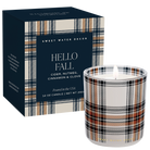 A lit 12 oz candle in a white glass jar with a beige, navy, black, and brown plaid pattern, shown next to its navy blue box featuring matching plaid trim. The brand 'Sweet Water Decor' is visible on both the box and the candle.